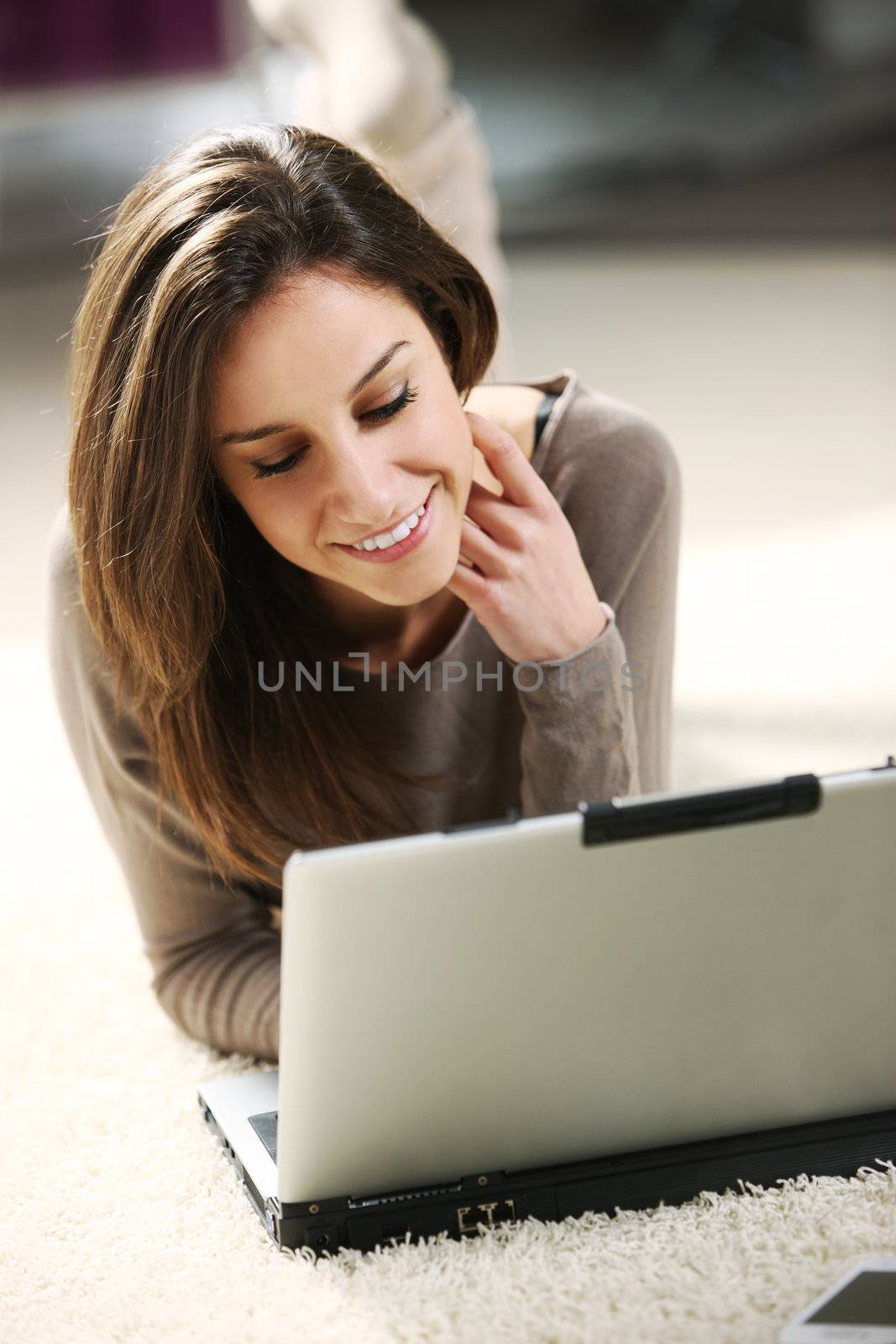 Smiling woman using her laptop in the living room. by stokkete