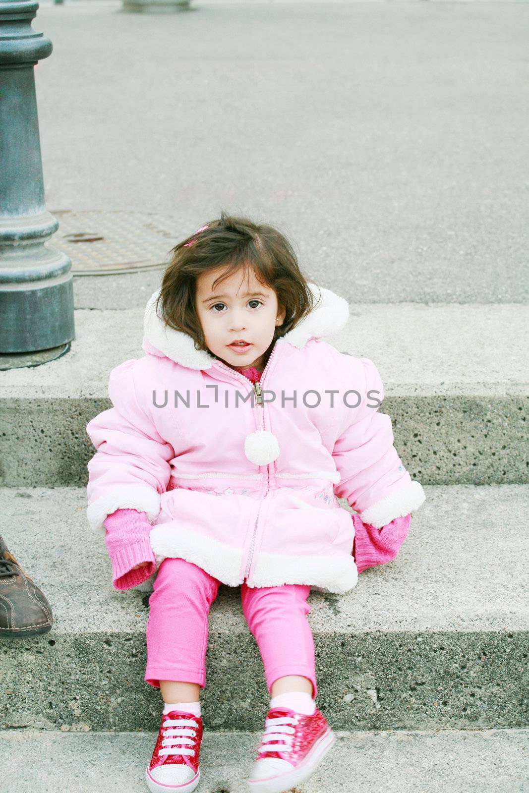 Little girl in winter clothes sitting in stairs looking at the c by dacasdo