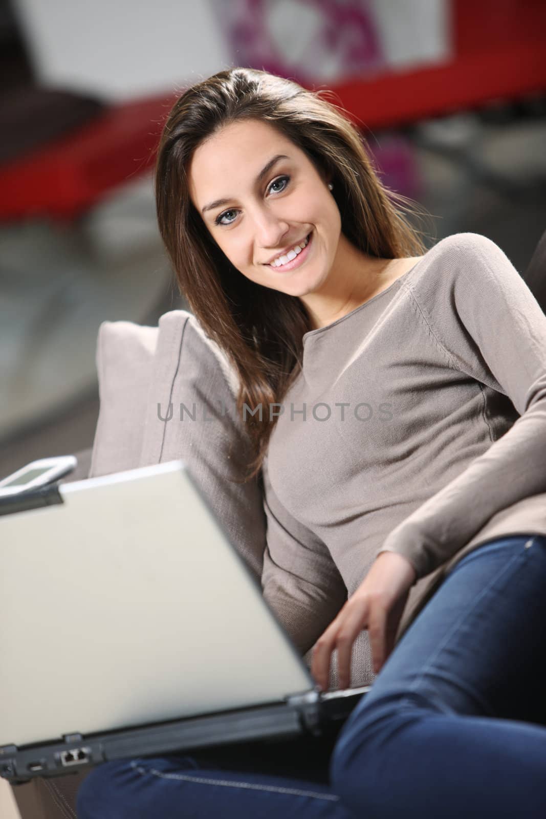 young woman at home, relaxing on a brown leather sofa with her laptop.