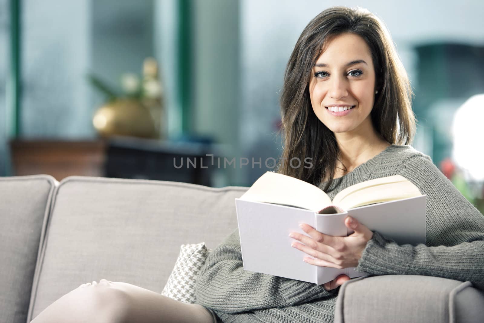 Portrait of a happy young woman lying on couch with book