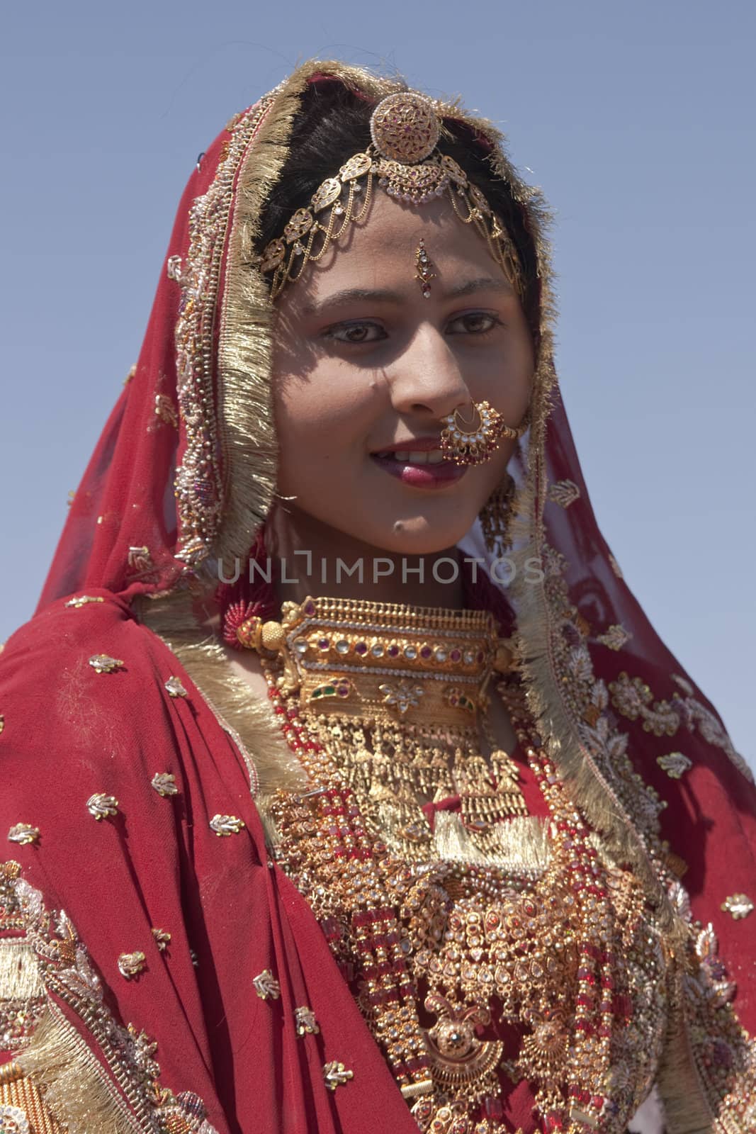 Indian lady dressed in ornate red sari and adorned with traditional Indian jewellery in Jaisalmer, Rajasthan, India.