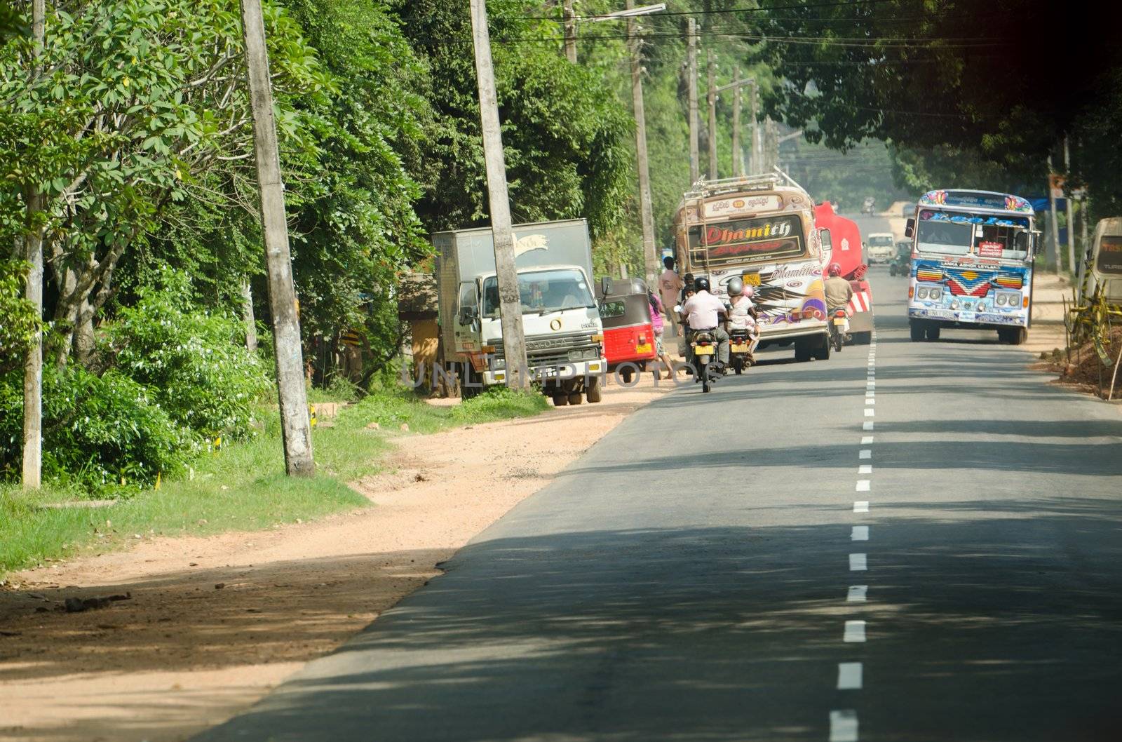 Habarana, Sri Lanka - December 6, 2011: Intensive traffic on a narrow asian street with regular buses covered by drawings, motobikes and cars.