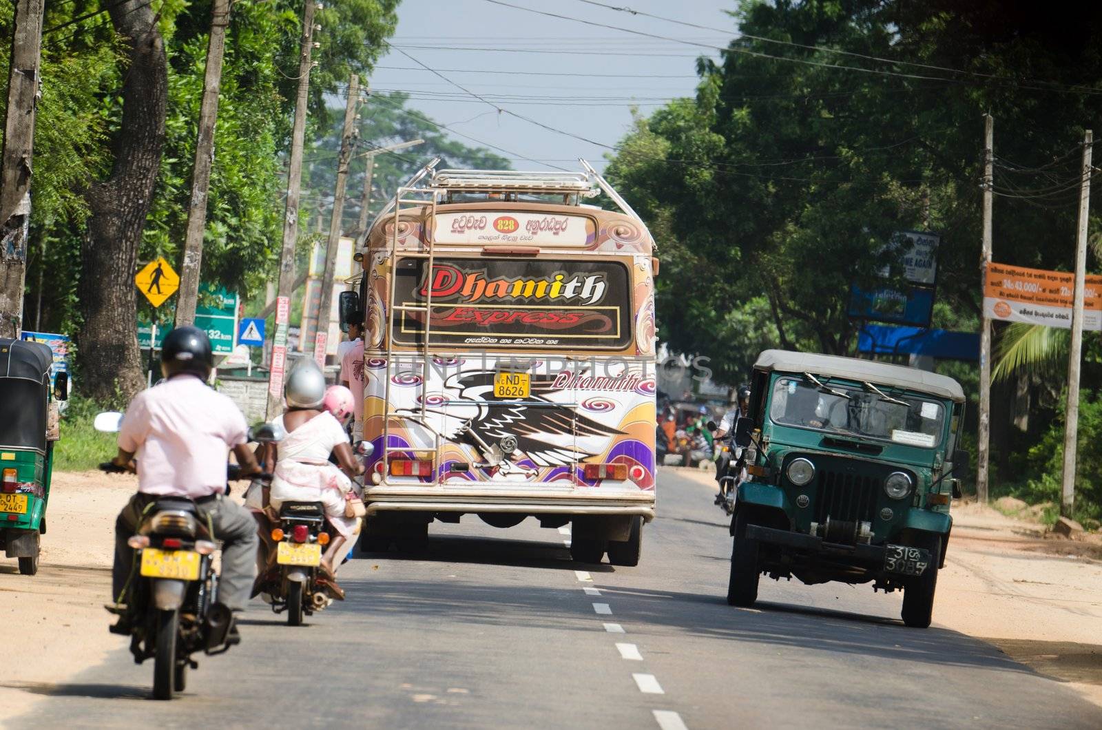 Habarana, Sri Lanka - December 6, 2011: Intensive traffic on a narrow asian street with regular bus covered by drawings, motobikes and car.