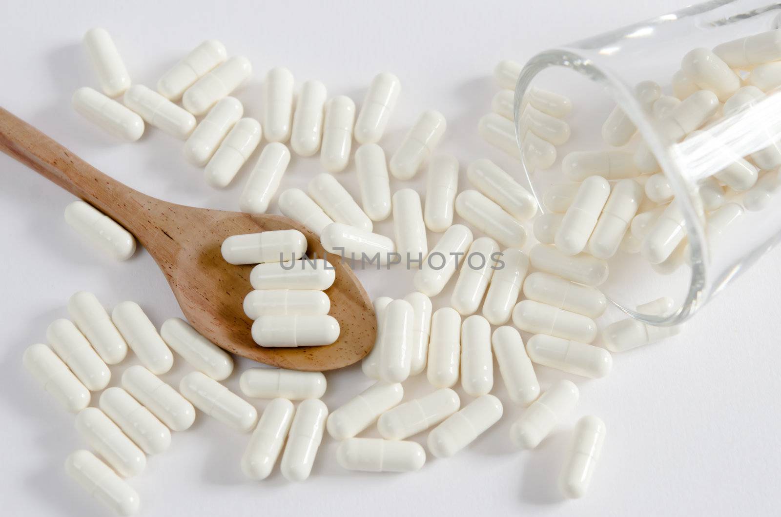 white pills spilling out of glass and pills on spoon