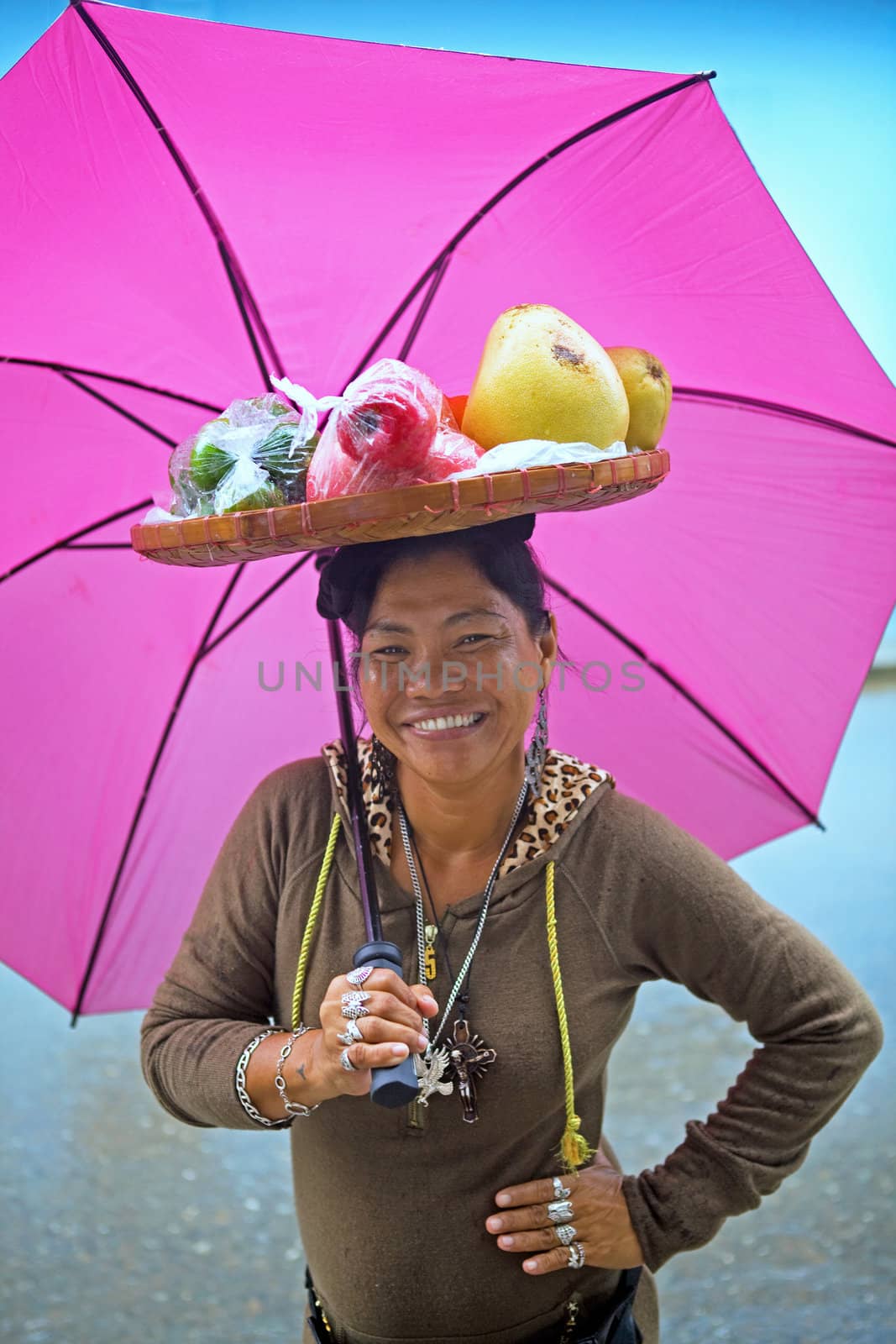 Smiling Filipino woman with a pink, magenta umbrella selling tropical fruit from a bamboo, woven basket balanced on her head in the Philippine Islands.