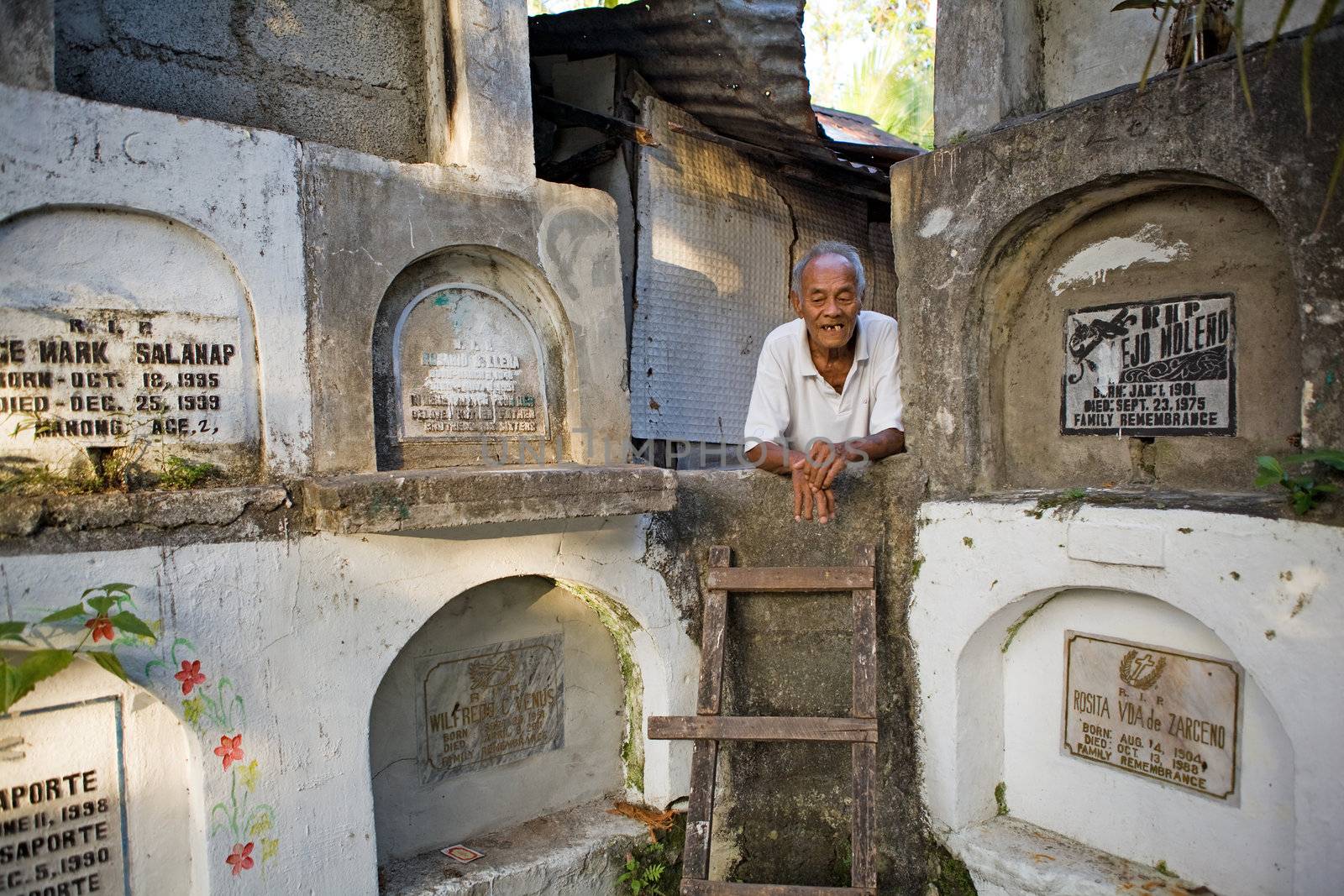 Bacolod City, Philippine Islands, March 2, 2012 - Homeless elderly Filipino man living among stacked concrete tombs in a cemetery.