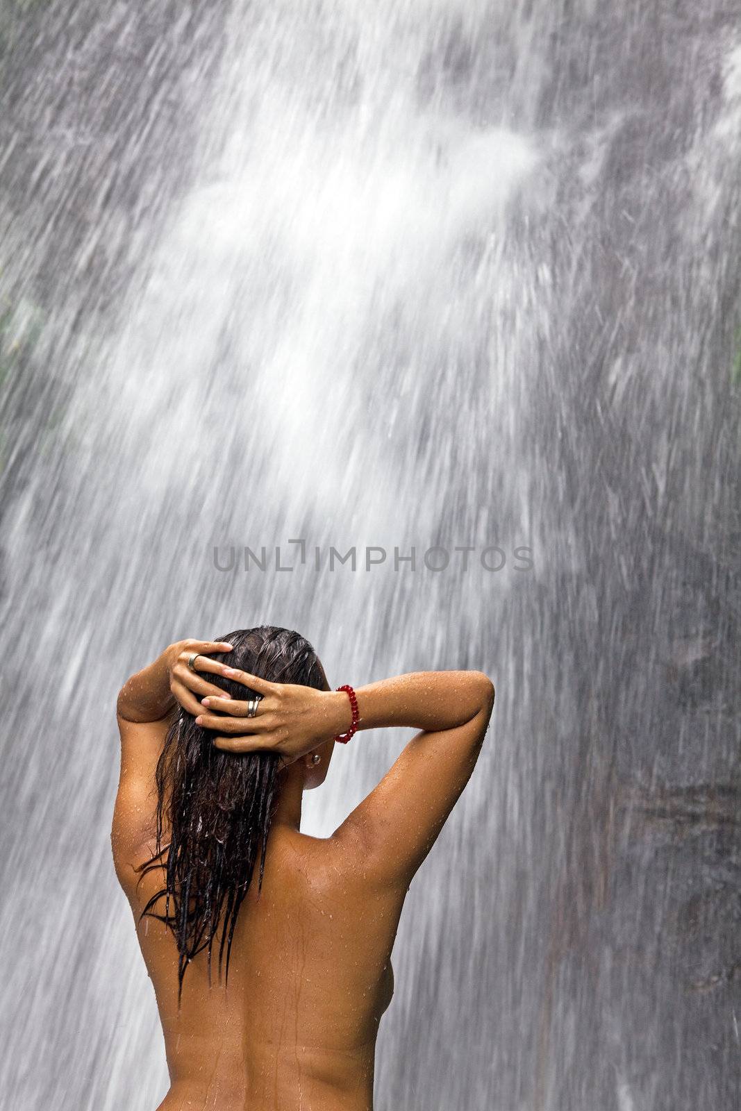 Semi-nude Filipino woman washing her hair and bathing in the spray of a waterfall at Pataan Mountain Resort in the Philippine Islands.