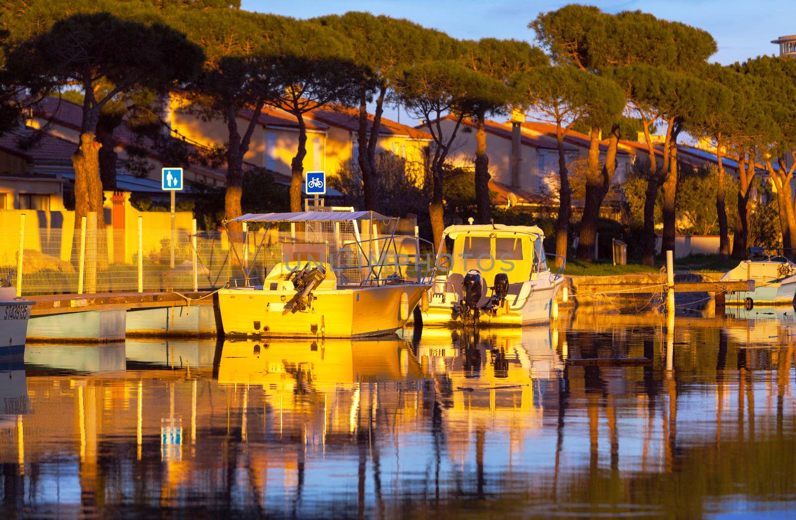 Small fishing and pleasure boats moored in a tranquil marina at sunset reflected in the golden glow of the sun