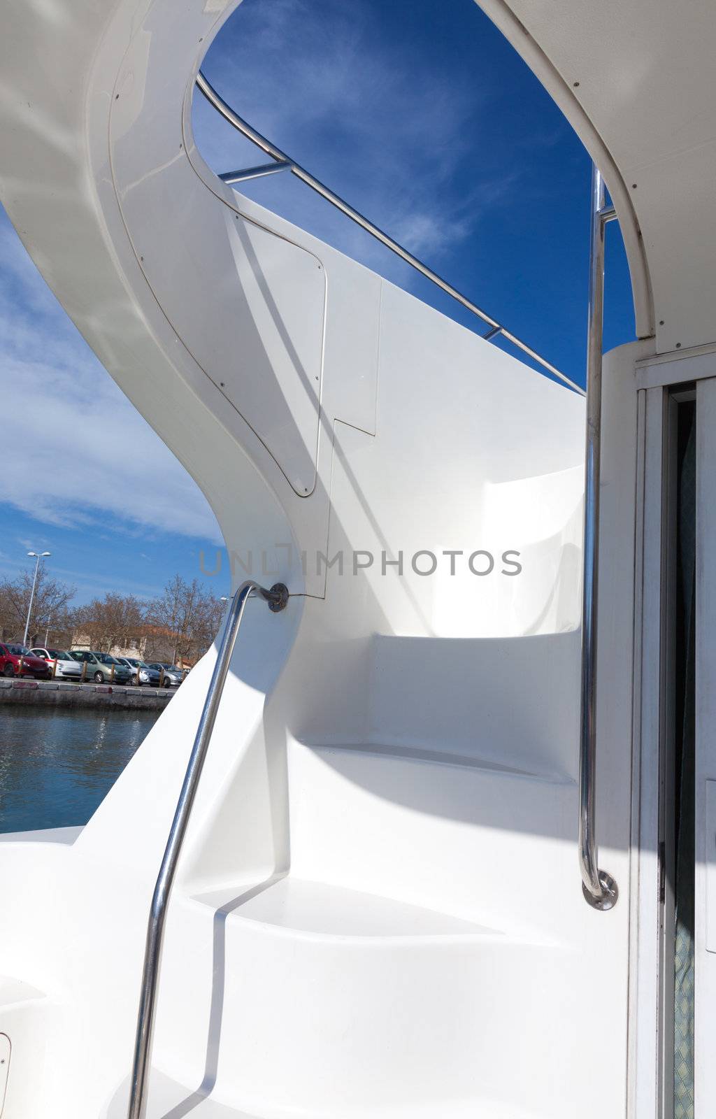 White steps on a luxury boat leading up to an upper deck with sunny blue sky through the arch of the hull