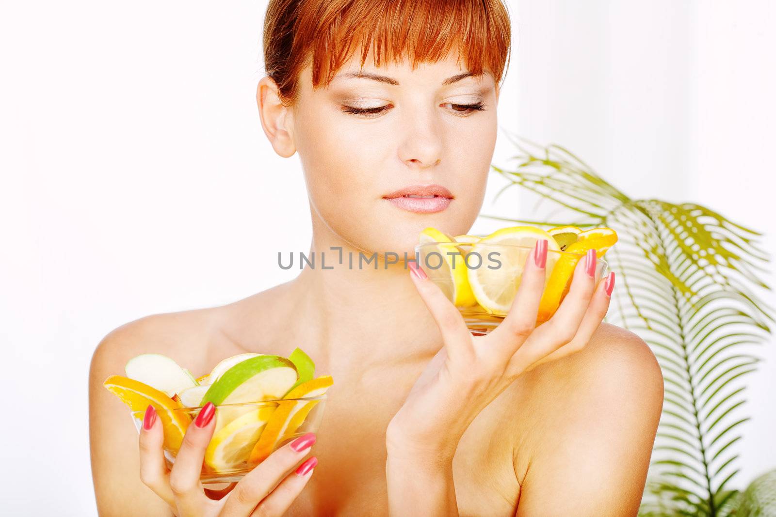 Pretty lady in a spa salon holding two bowls with fruits and looking in one