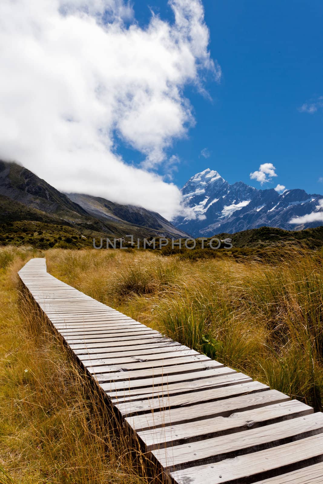 Boarded trail section in Hooker Valley on a track leading to Aoraki, Mount Cook, highest peak of Southern Alps, an icon of New Zealand partially covered in clouds