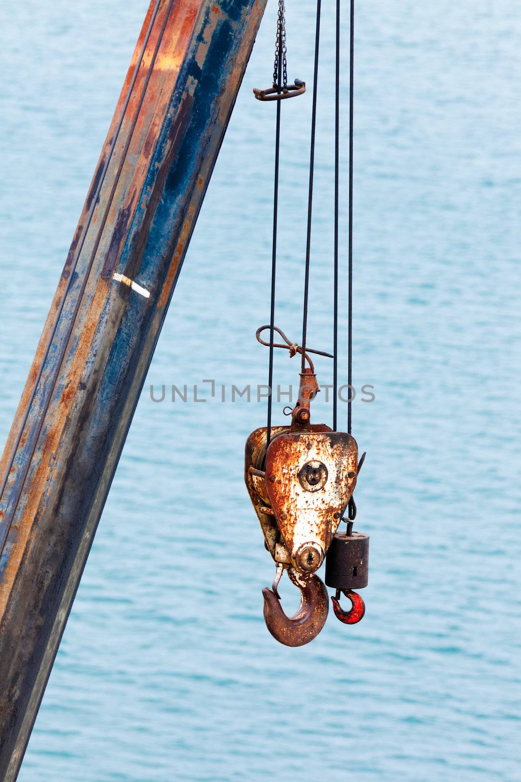 Two different sized battered and rusted hooks and cables of crane for hoisting or lifting heavy loads in harbor against blurry ocean background