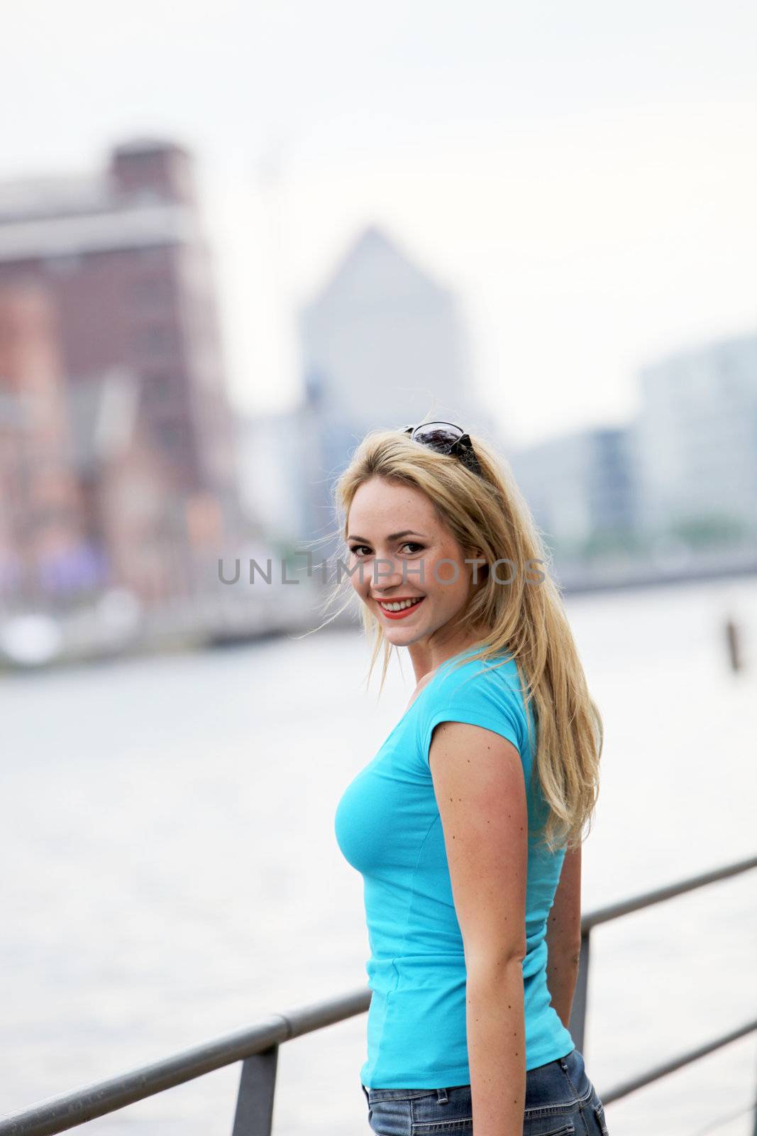 Young smiling female tourist looking back over her shoulder at the camera as she stands alongside an urban river 