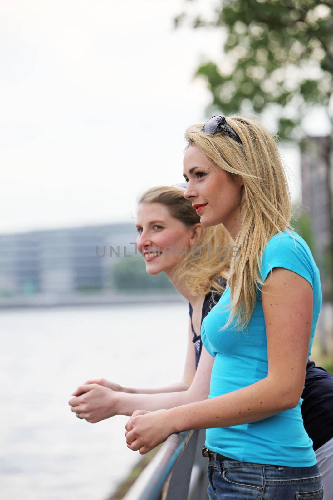 Two women friends stand at a railing overlooking a river and enjoy a moment of peace and tranquillity together 