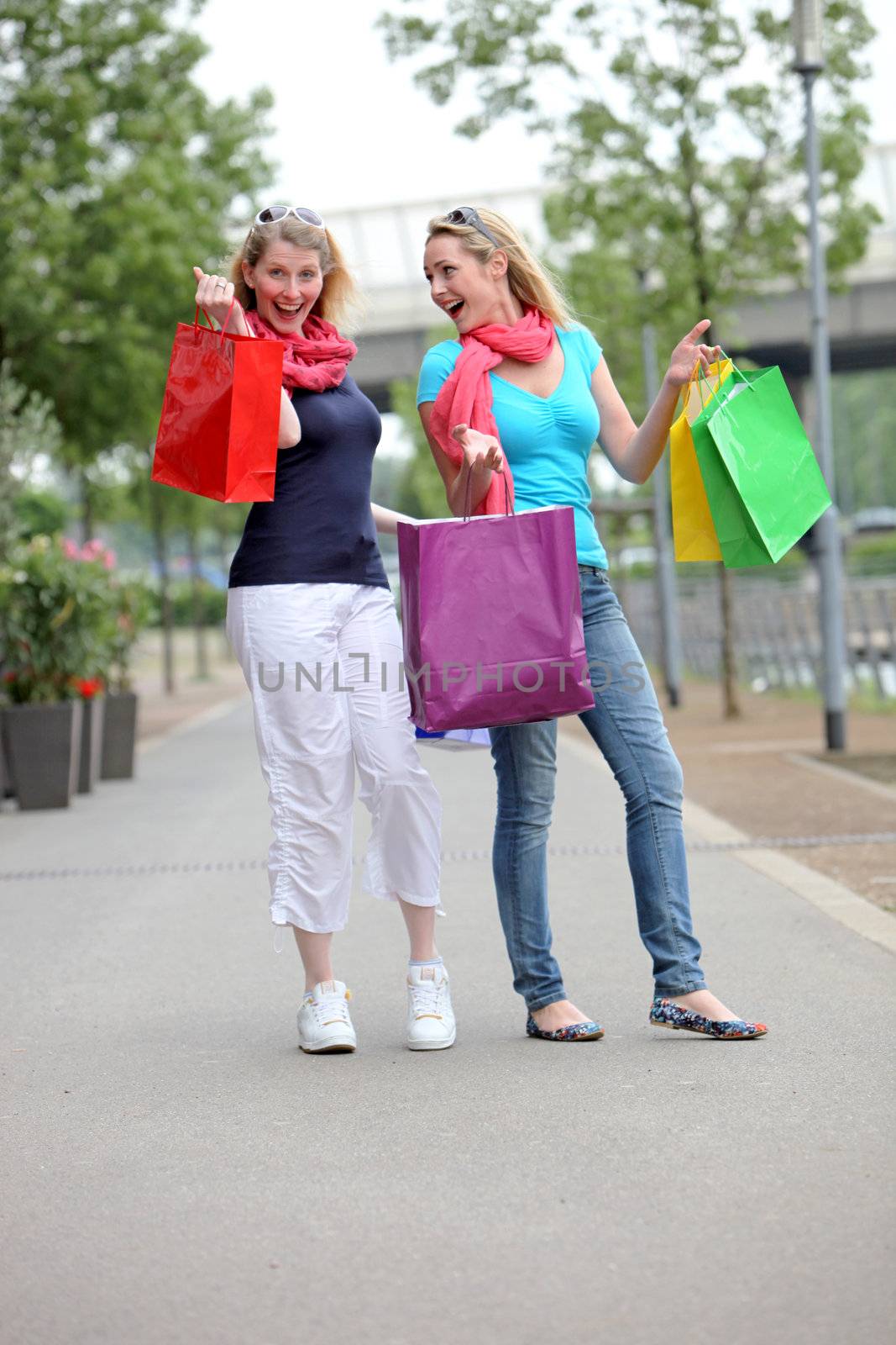 Excited women with their purchases in colourful carrier bags laughing on the sidewalk 