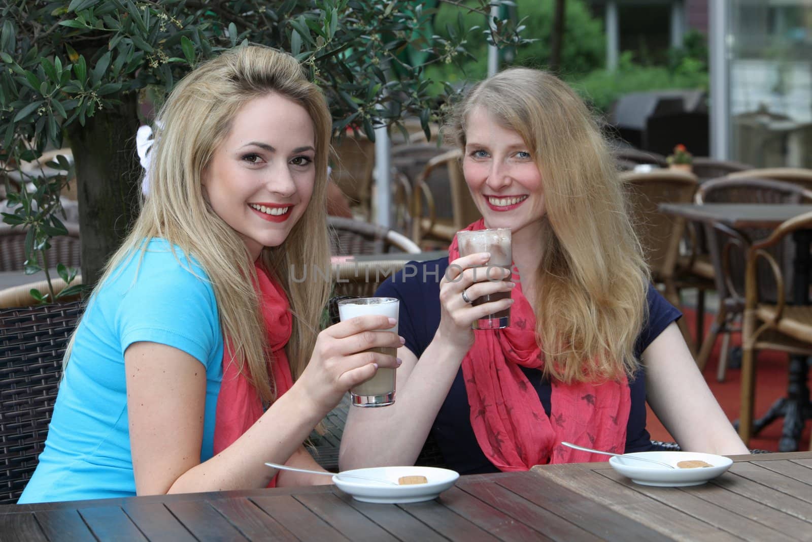 Attractive stylish female friends enjoying a refreshing glass of iced coffee together seated at a table in an open-air cafe