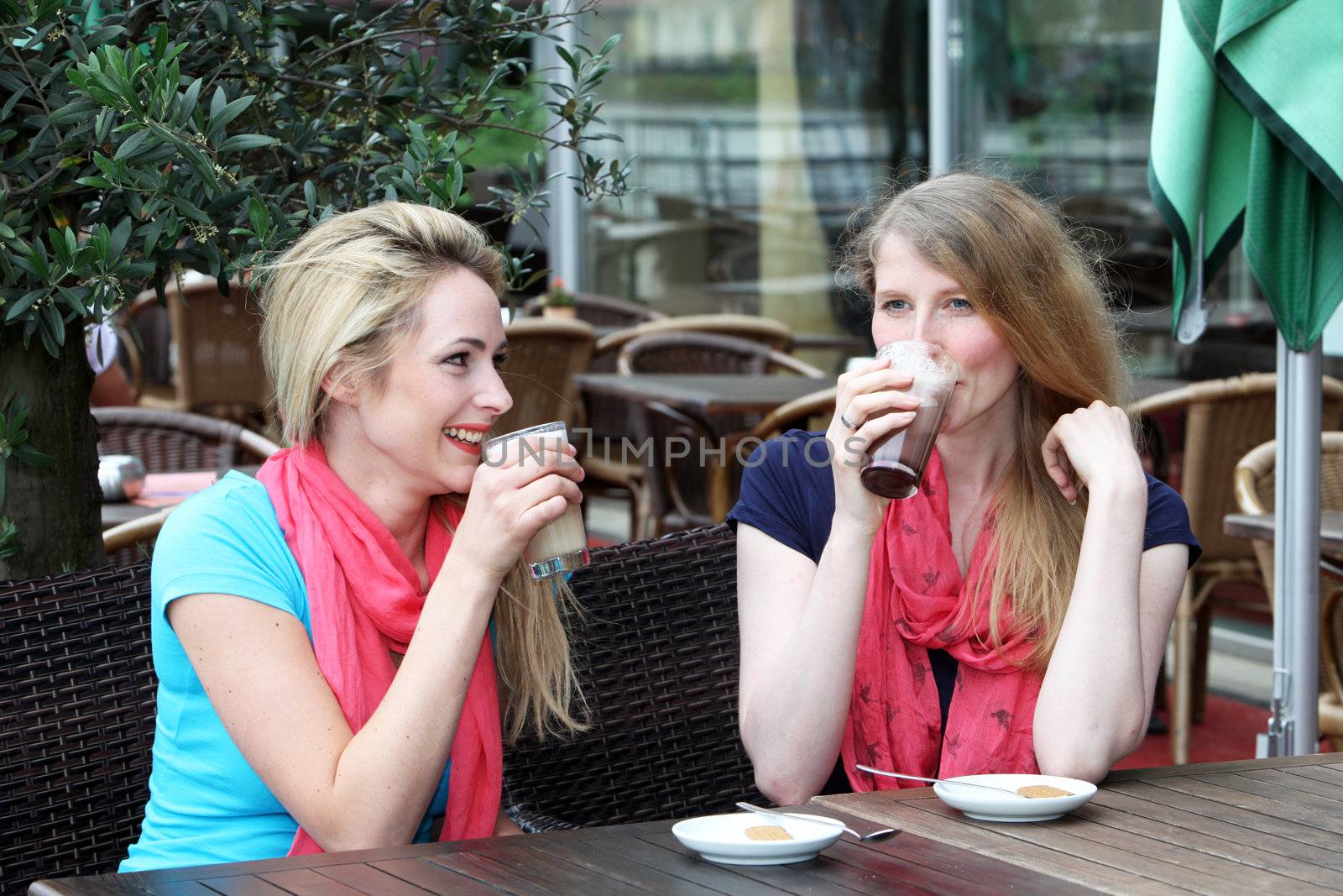 Two stylish woman enjoying a cool refreshing drink seated at an outdoor restaurant table 