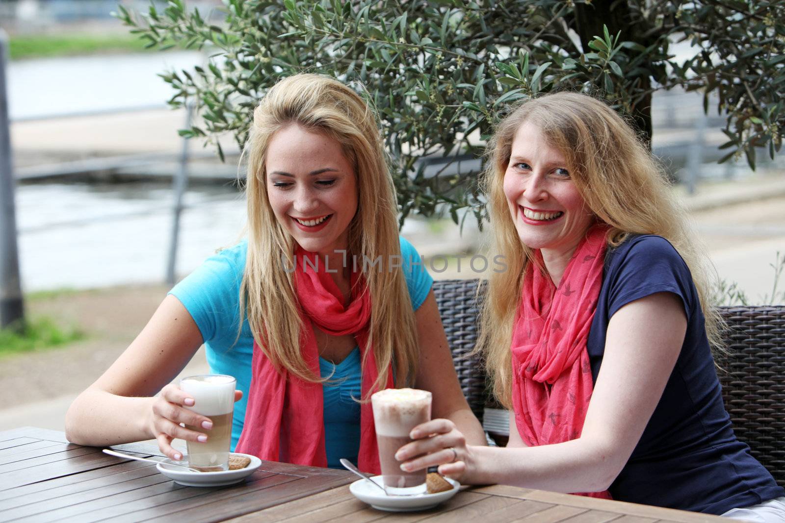 Two attractive stylish female friends relaxing over drinks seated at a table at an open-air restaurant Two attractive stylish female friends relaxing over drinks seated at a table at an open-air restaurant