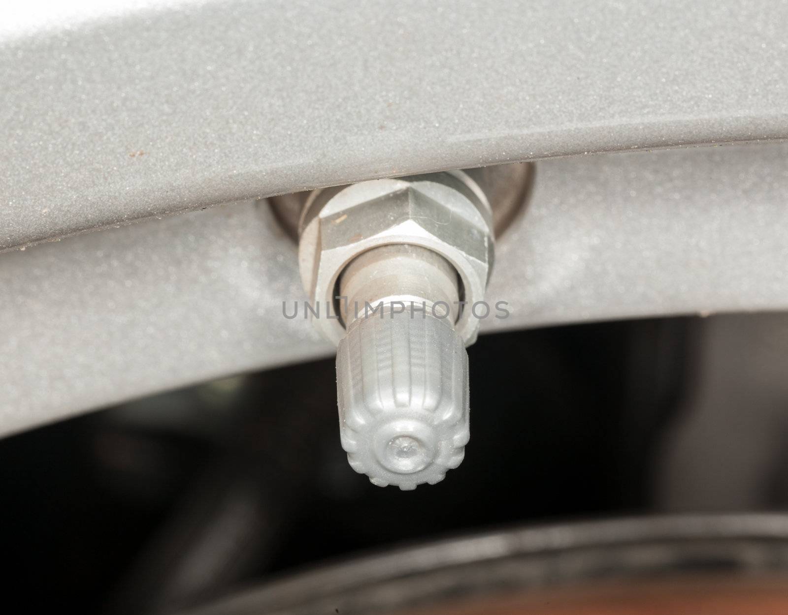 Silver colored tyre pressure valve on alloy wheel of car