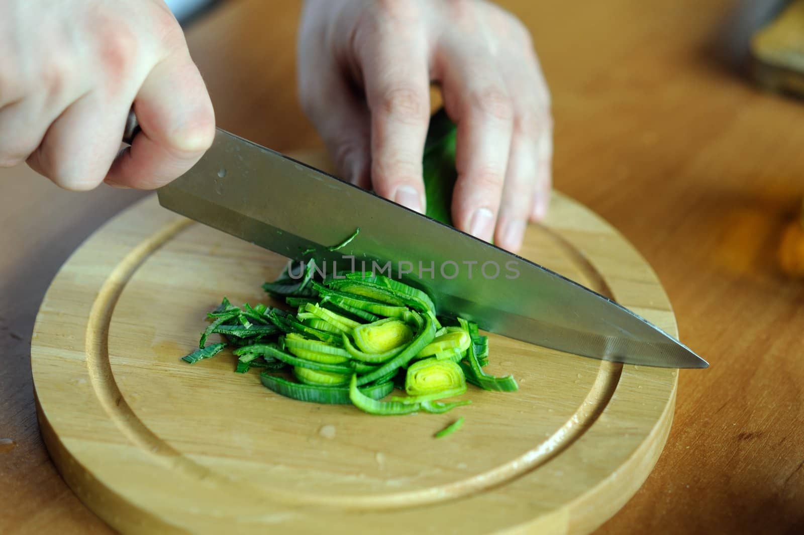 An image of hands cutting green leek on the board