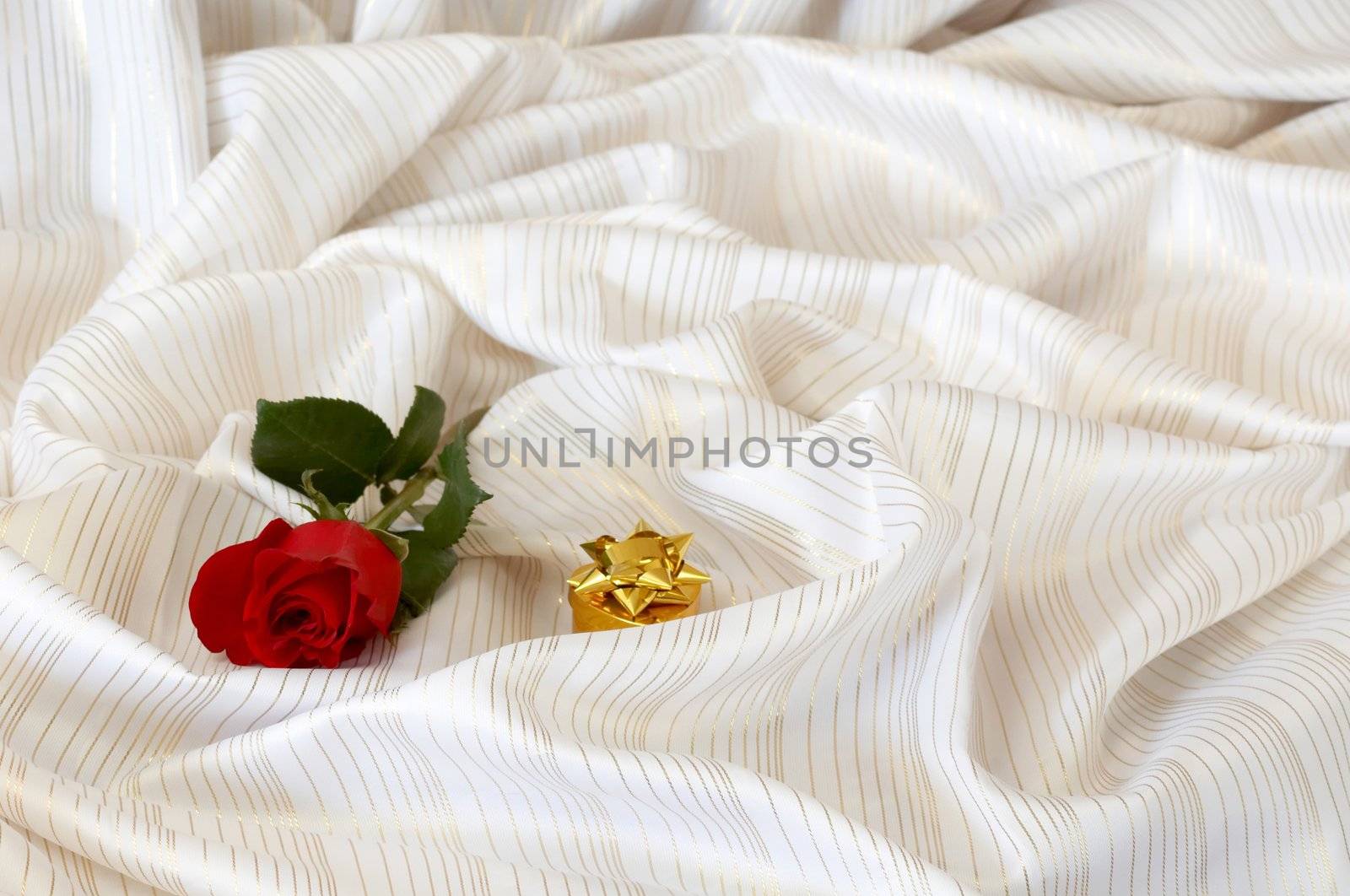 Red rose and jewelry on background of fabrics