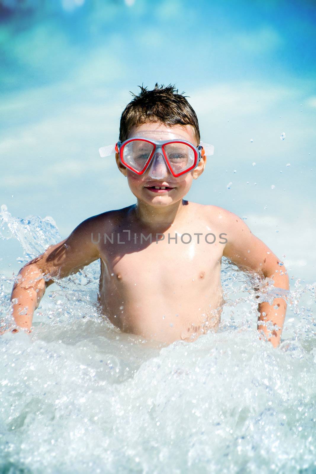Child sitting in water waves and looking at camera