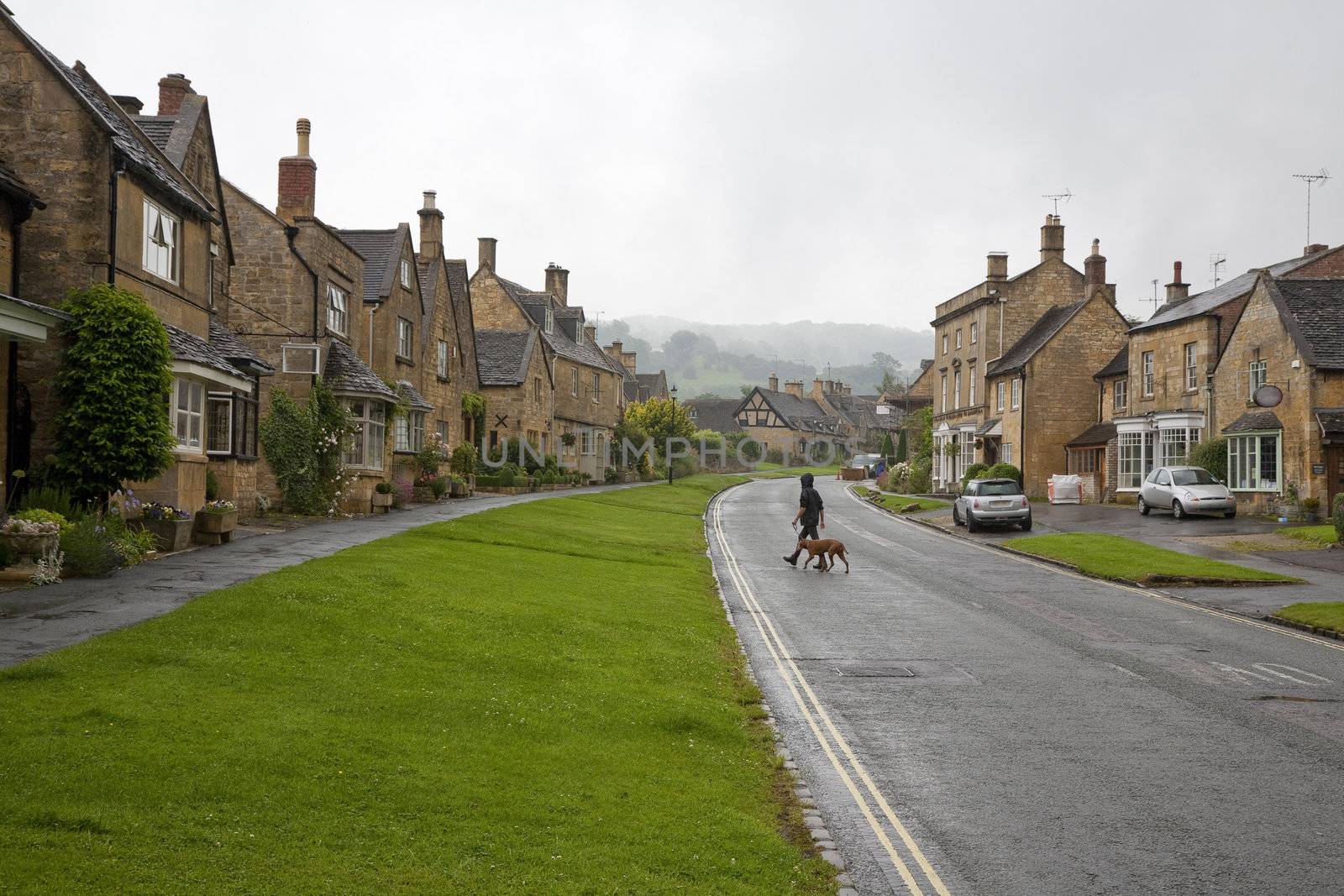 Teenager walking the dog in the picturesque village of Broadway, Cotwold, United Kingdom while it is raining.