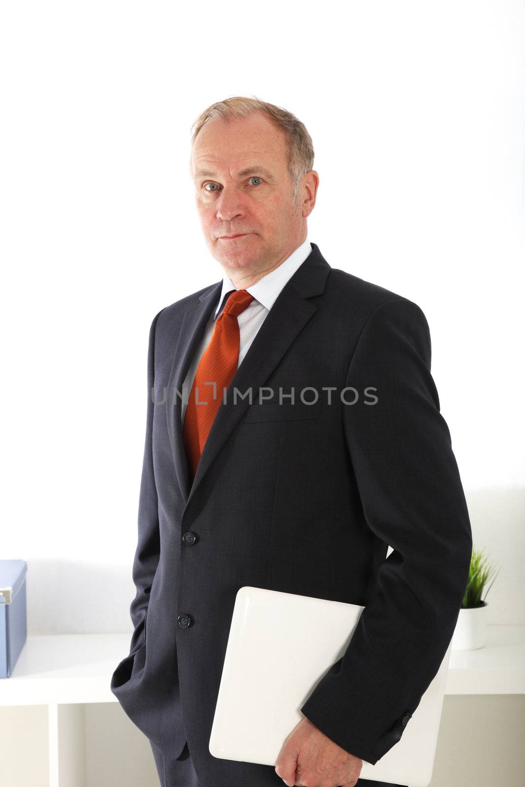 Company director or senior businessman standing proudly with a laptop under his arm and his other hand in his pocket 