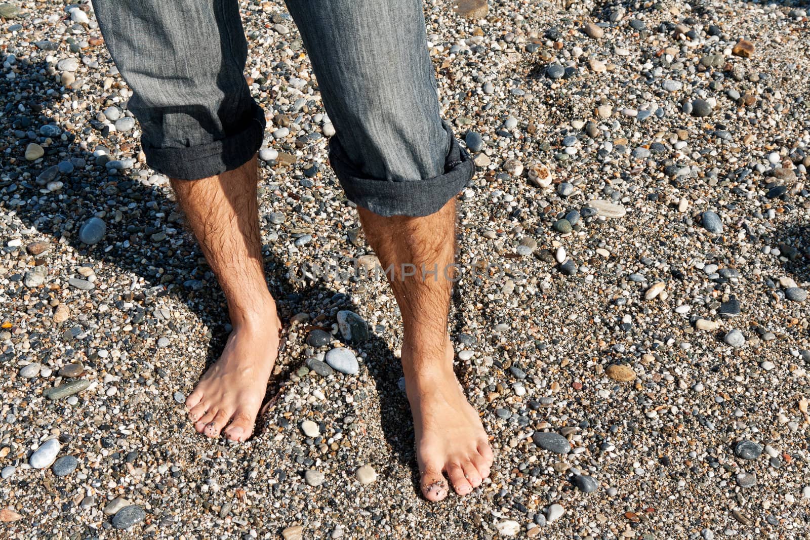 pair of men's feet on the beach with pebbles