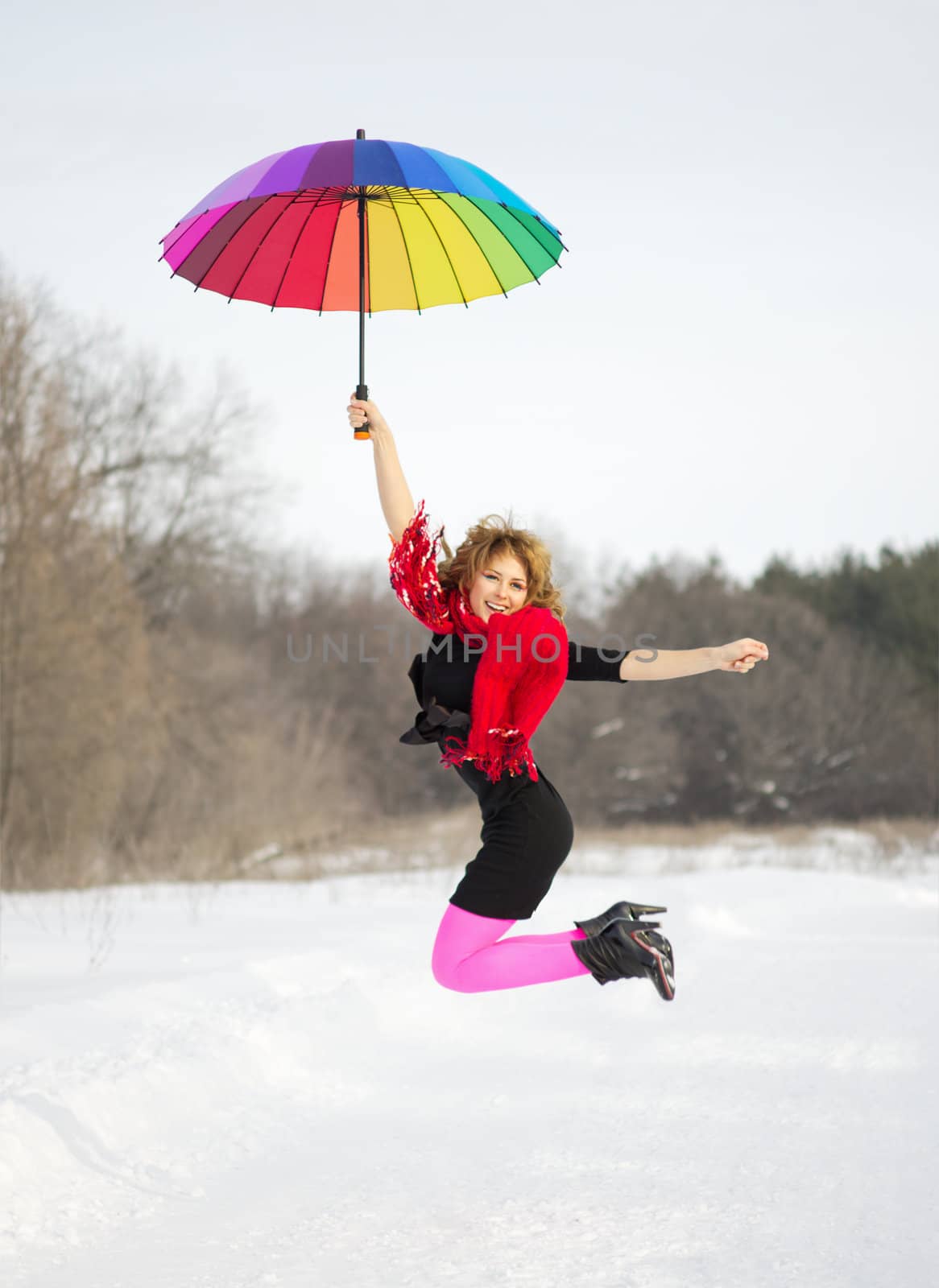 Jumpling young woman with multicolor umbrella at winter forest