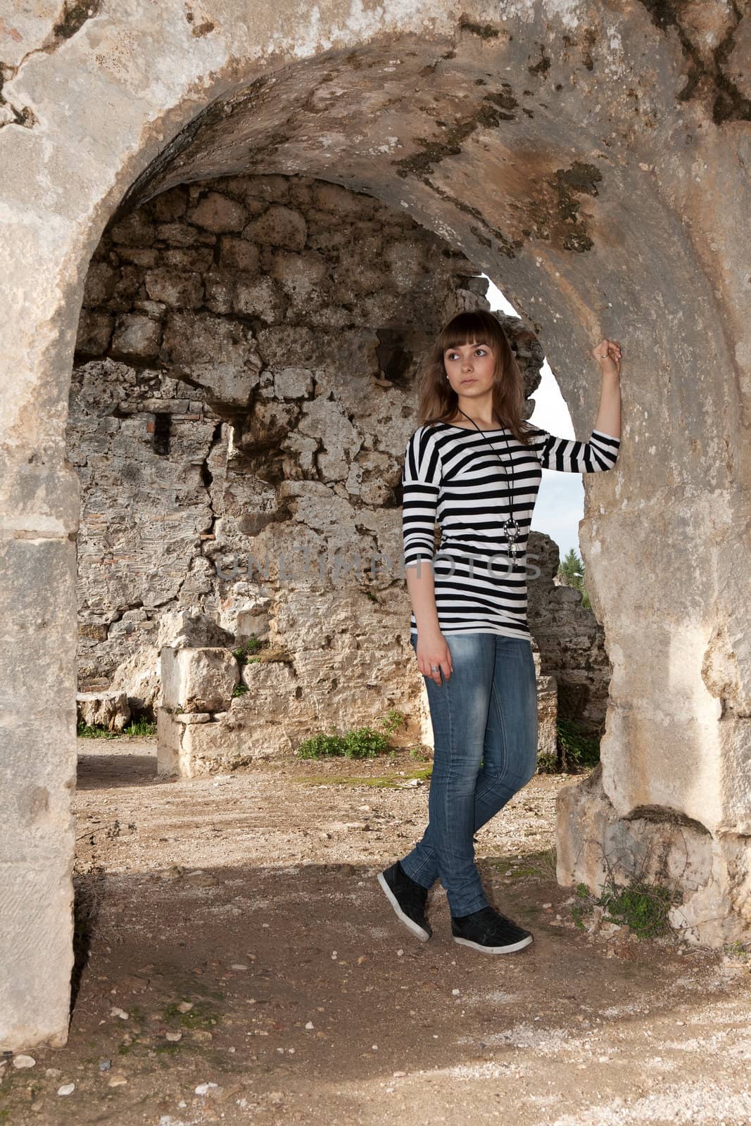 Young girl in jeans in an arch in the ruins