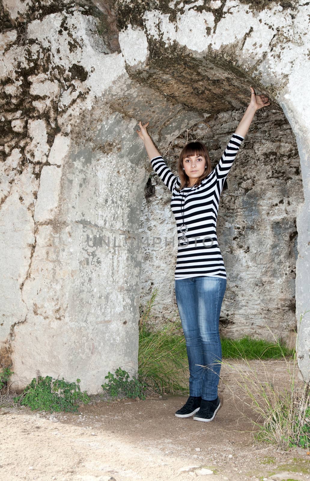Young girl in jeans in an arch in the ruins
