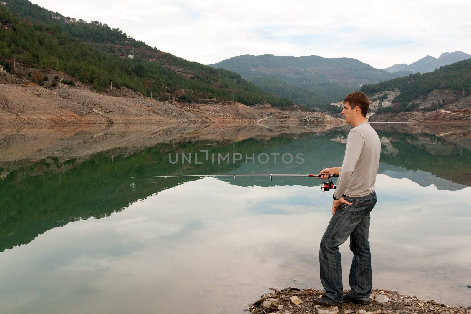 man with a fishing rod on the bank of a mountain lake