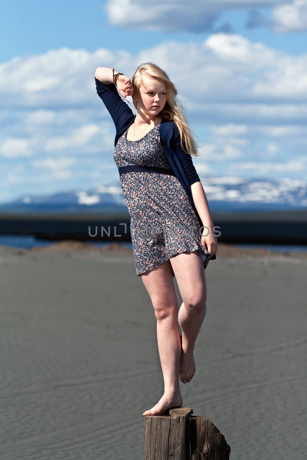girl standing on one leg on a wooden post against the sky and mountains