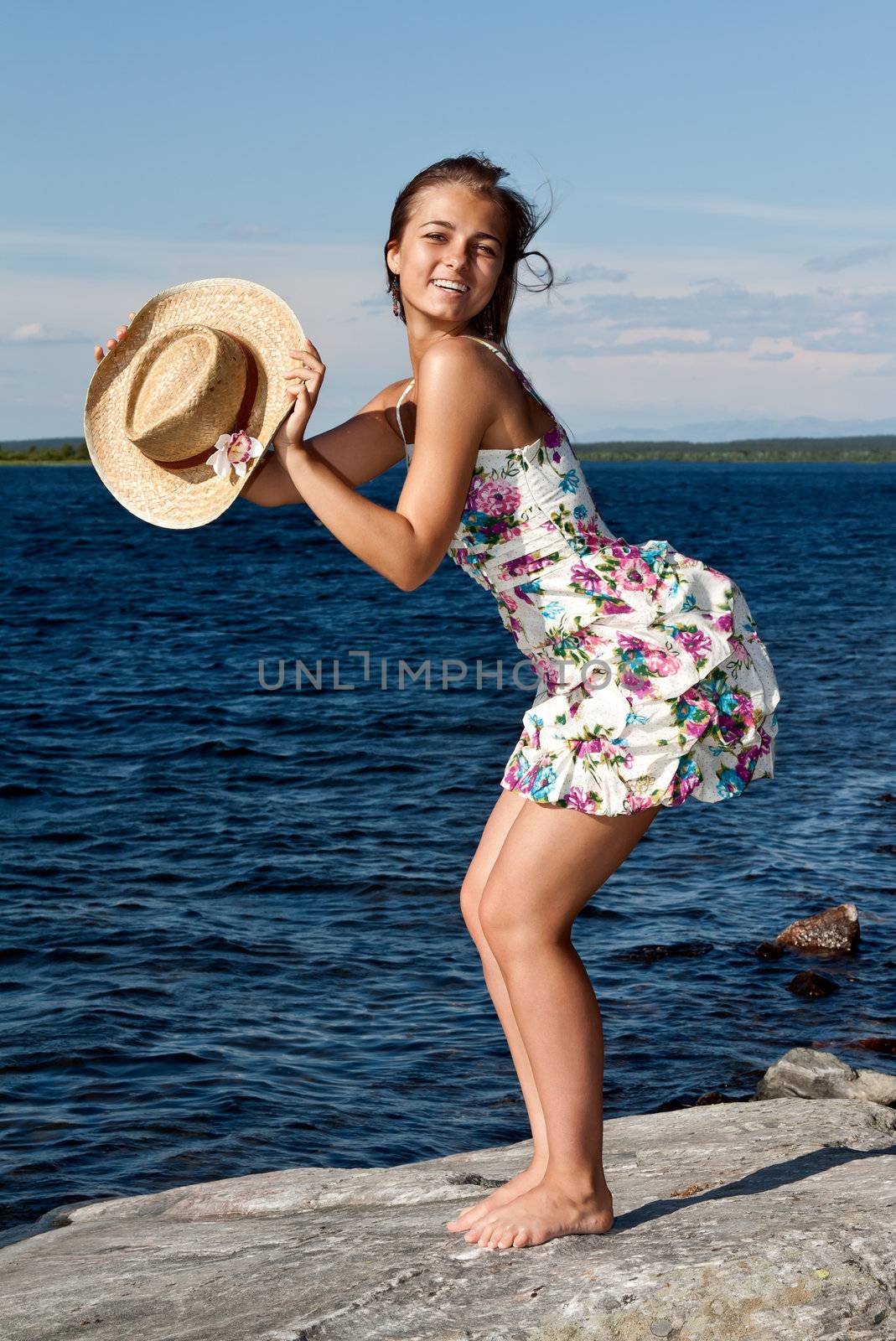 girl with a straw hat standing on a rock by the lake