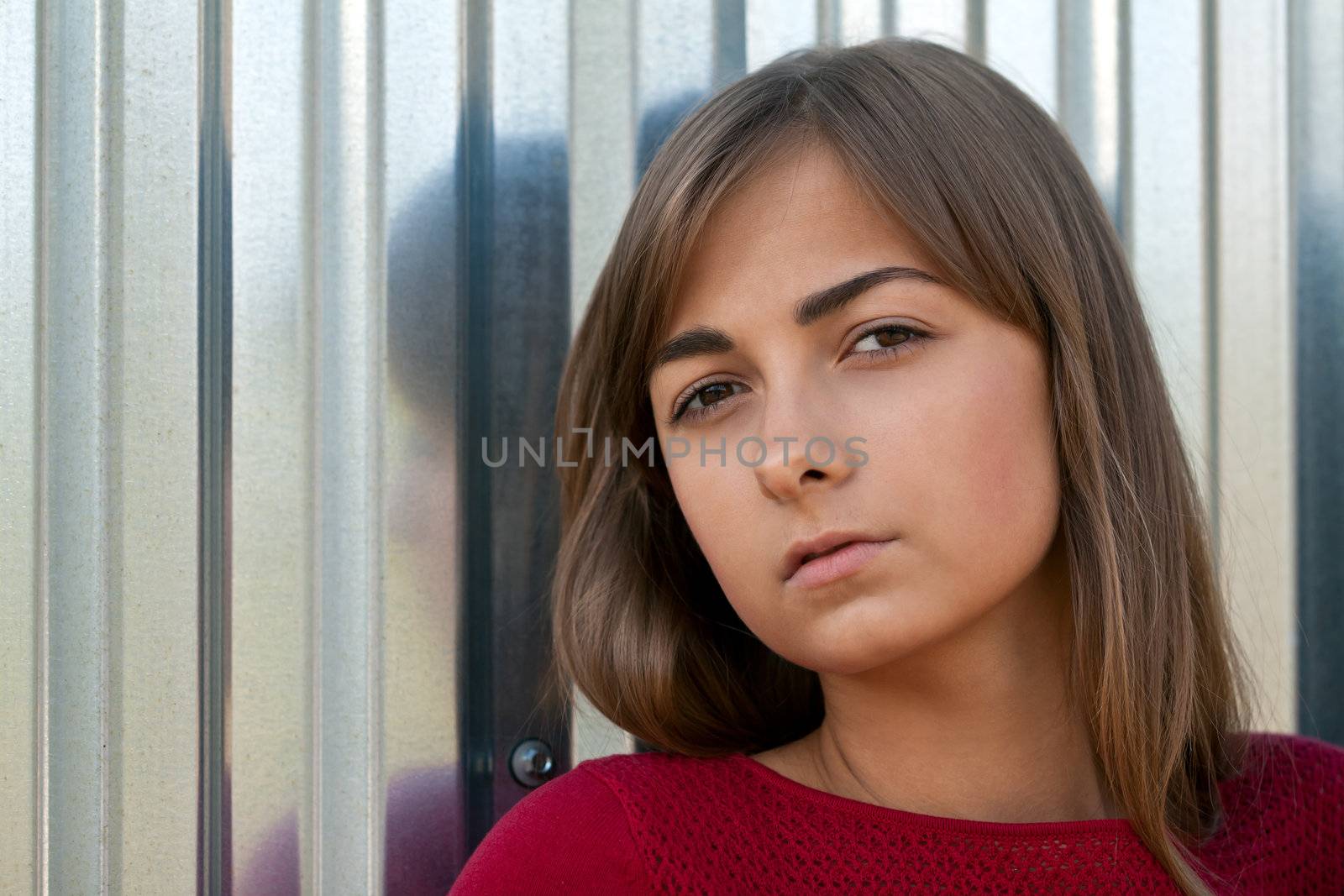 Portrait of a beautiful young girl in a red dress against the iron wall