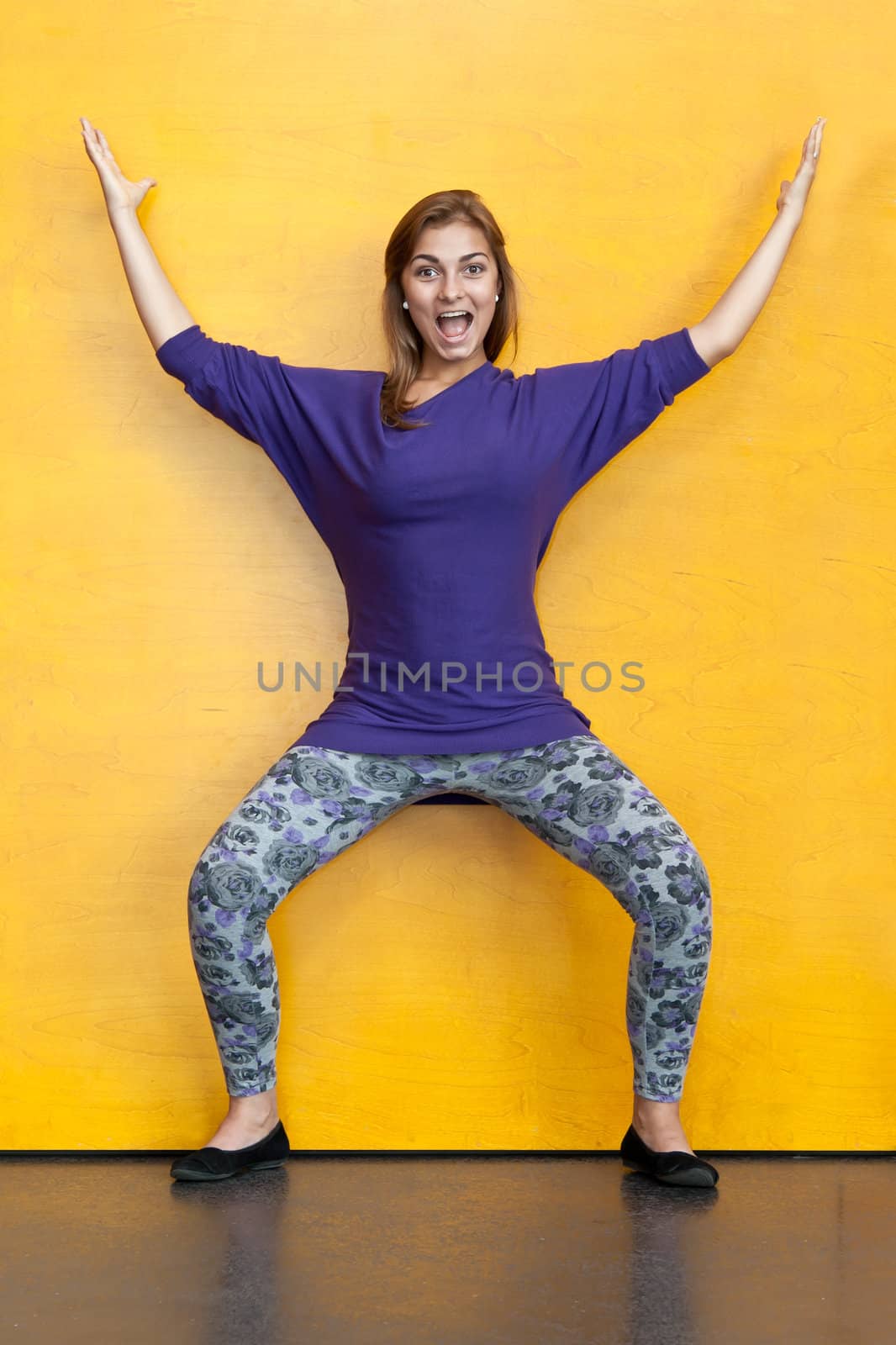 Beautiful girl in purple sweater on a background of yellow wood wall