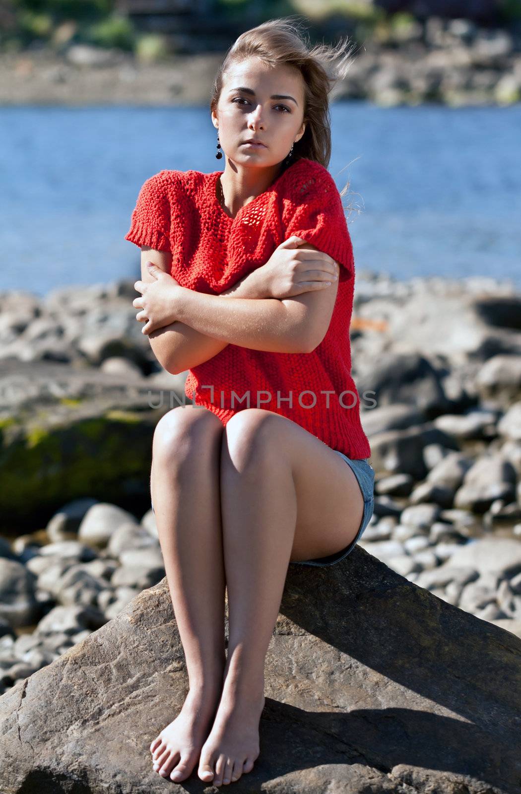 girl badly frozen sitting on a rock in a red sweater against the rocky shore of the White Sea