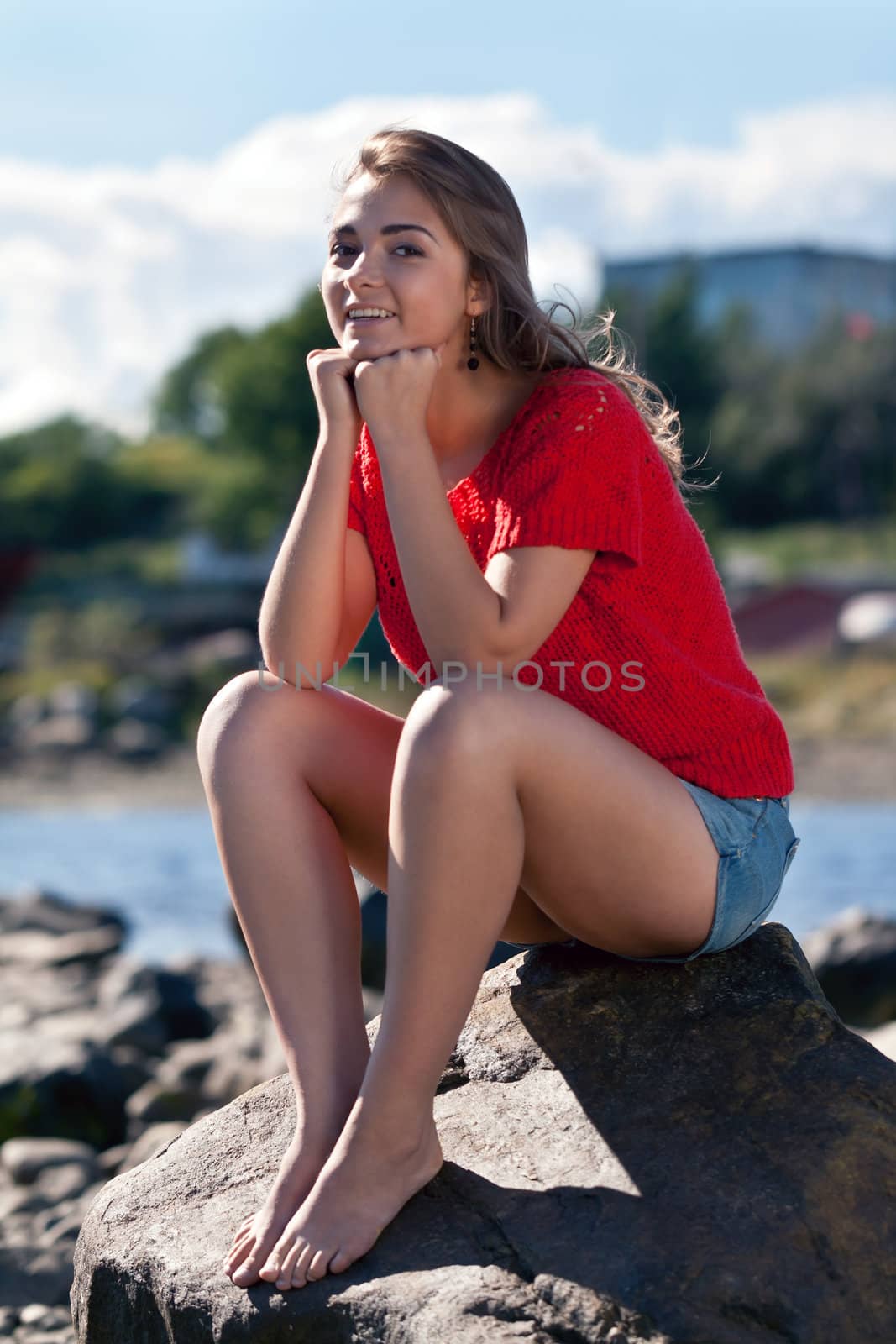 girl in a red sweater sits on a rock against the backdrop of the coastline