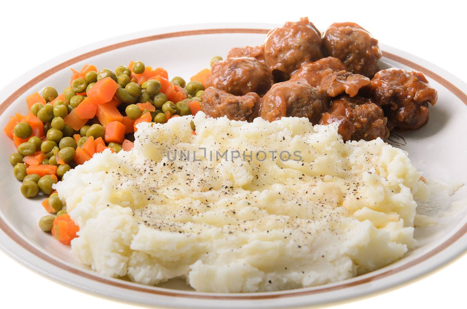 An american supper of mashed potatoes, with sweet and sour meatballs with peas and carrots.