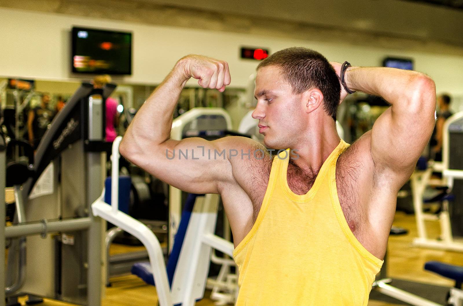 Handsome bodybuilder showing his muscular arms in gym