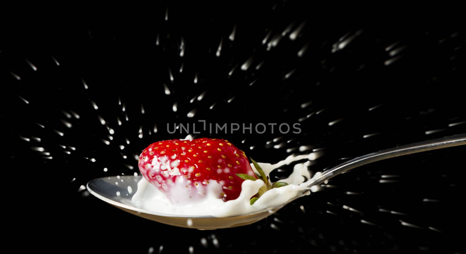 red, ripe strawberry falling in spoon with milk by gewoldi