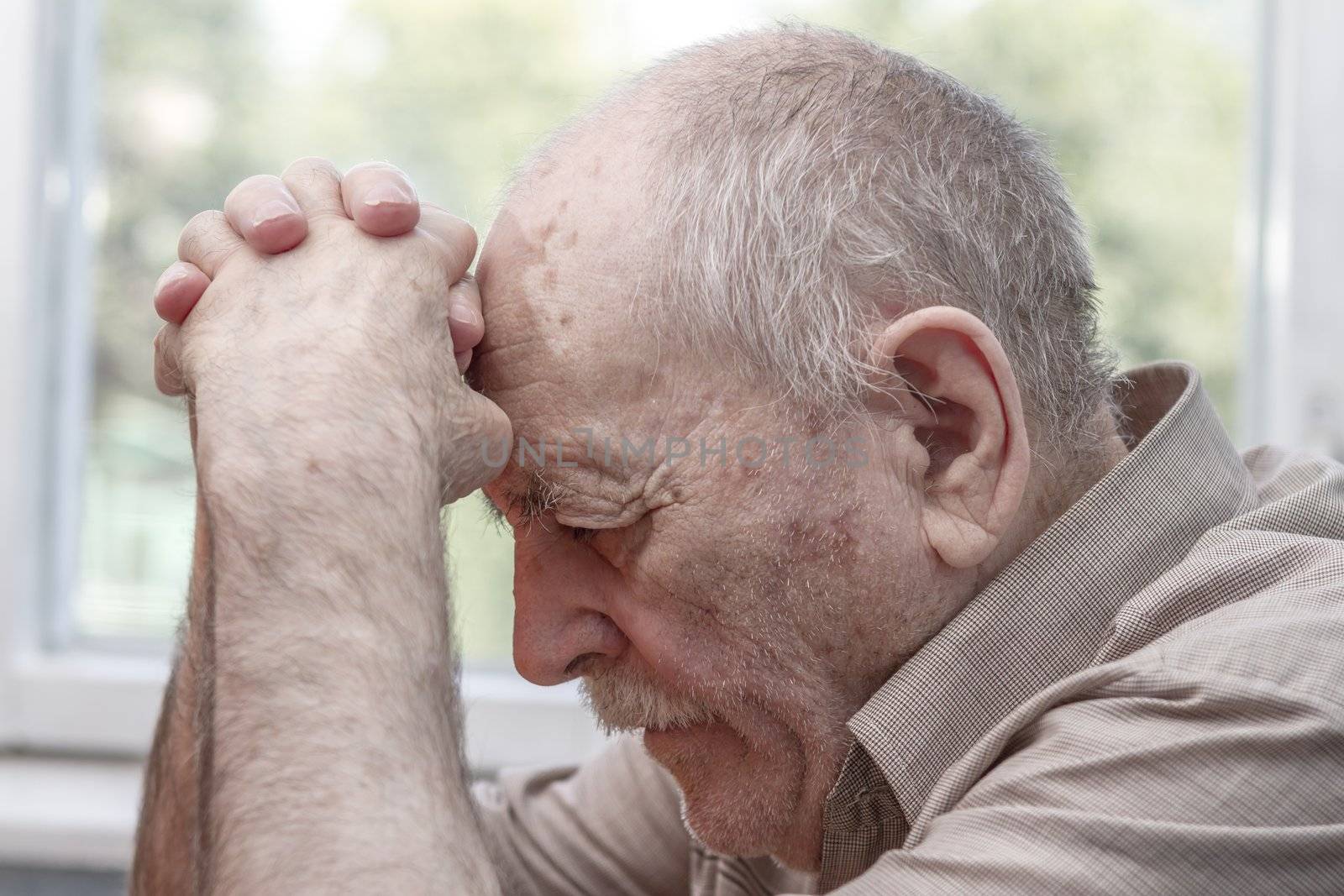 Old man praying at home near the window