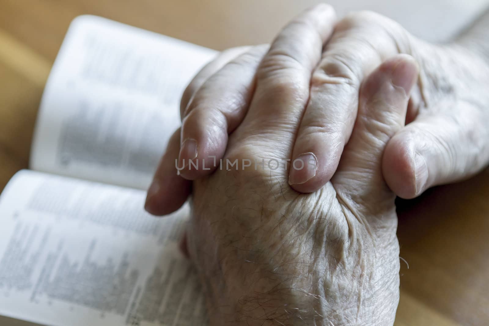 weathered old man's hands clasped in prayer over open Bible
