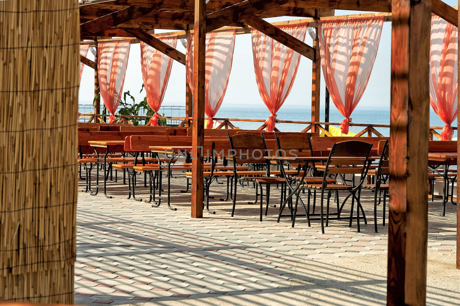 View out across a sunny open-air wooden deck with restaurant tables and chairs to the ocean beyond