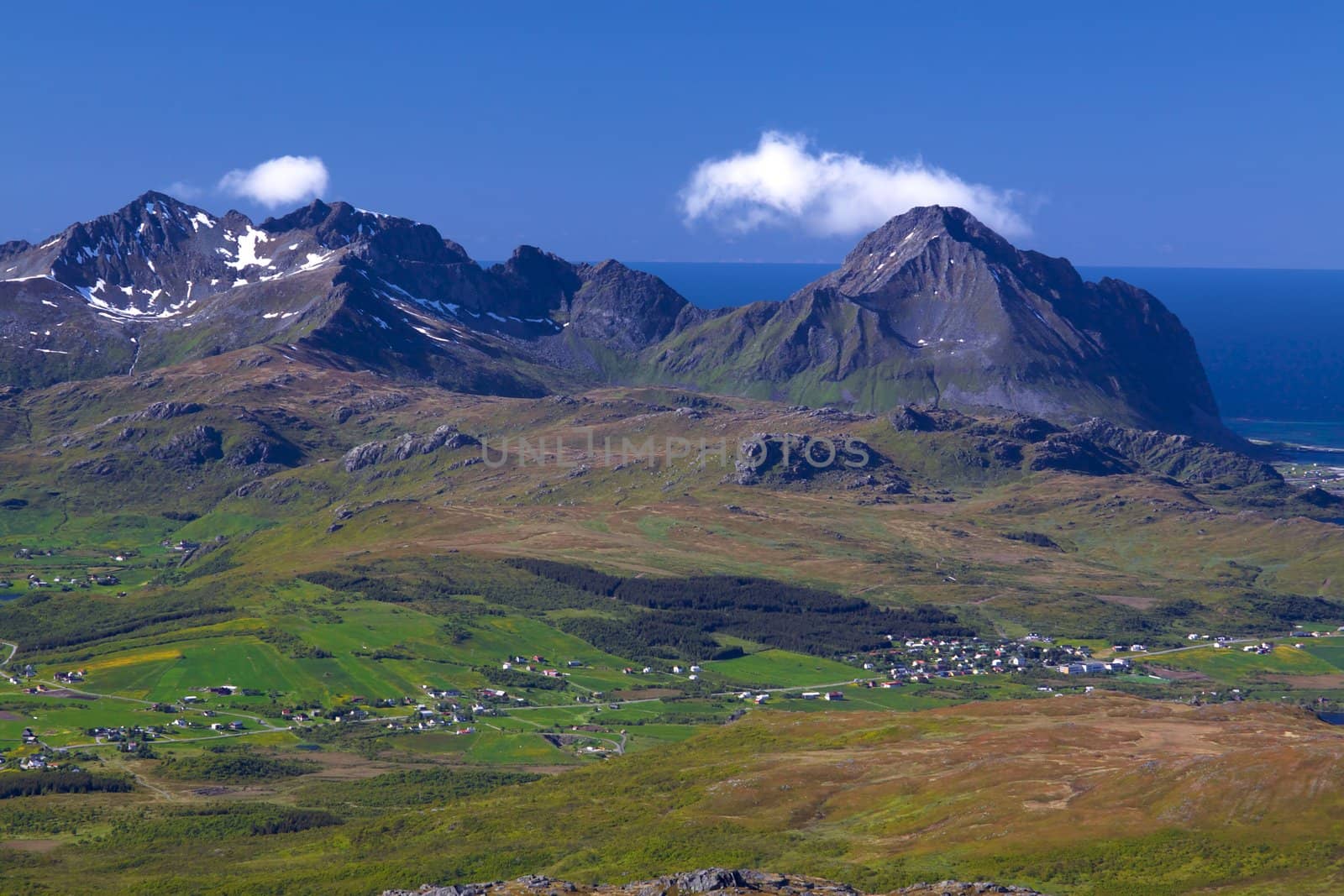 Picturesque panorama on Lofoten from Justadtinden with green lowlands, snowy peaks of mountains and Atlantic ocean in the background