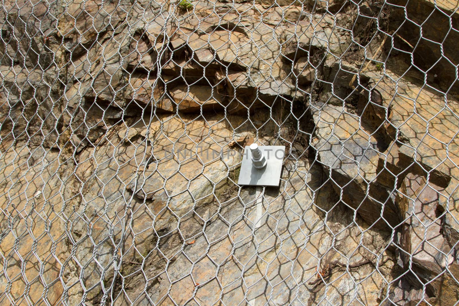 Metal safety netting covering loose shale rock with a square washer and steel nut and bolt fixing.