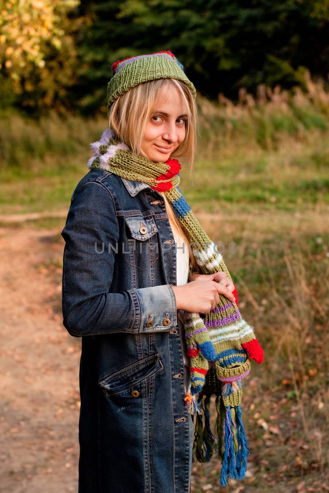 A standing girl in a cup and scarf and mittens and jeans coat in a forest
