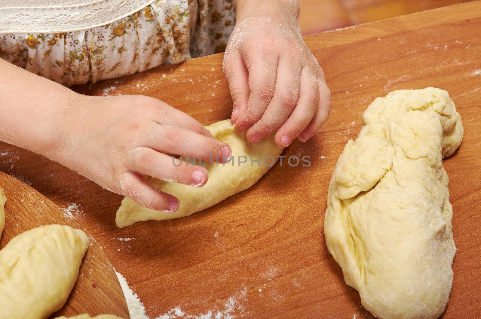 Smiling little girl kneading dough at kitchen .Detail of hands kneading dough