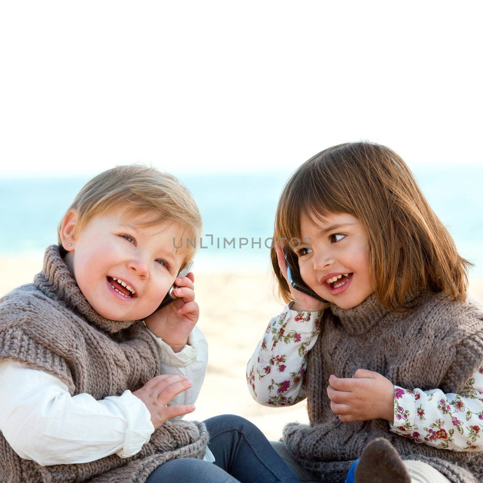 Portrait of two cute little girls o beach talking on mobile phones.